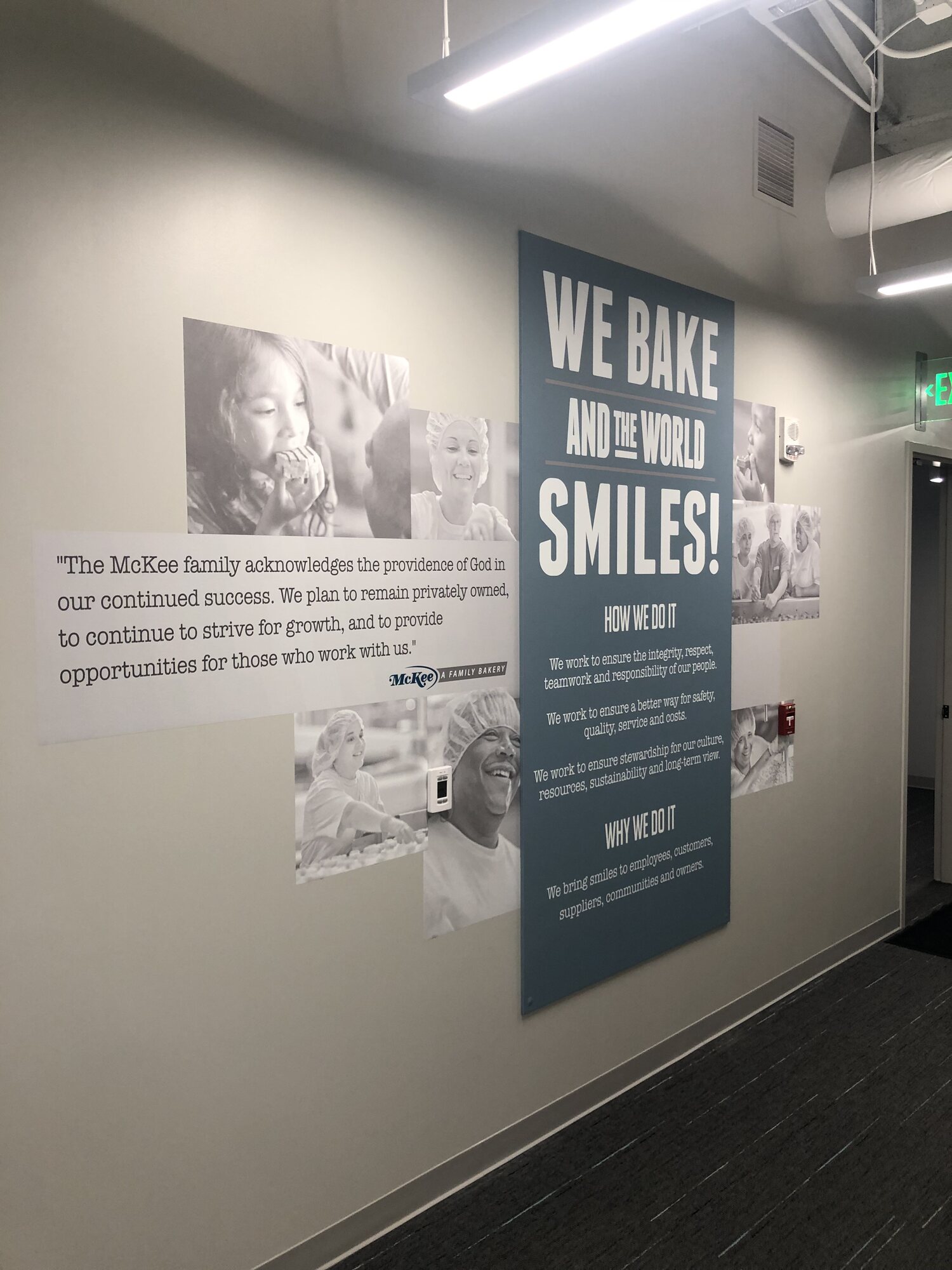 McKee Foods hallway wall display with a blue “We bake and the world smiles!” panel, company quote and black-and-white employee photos