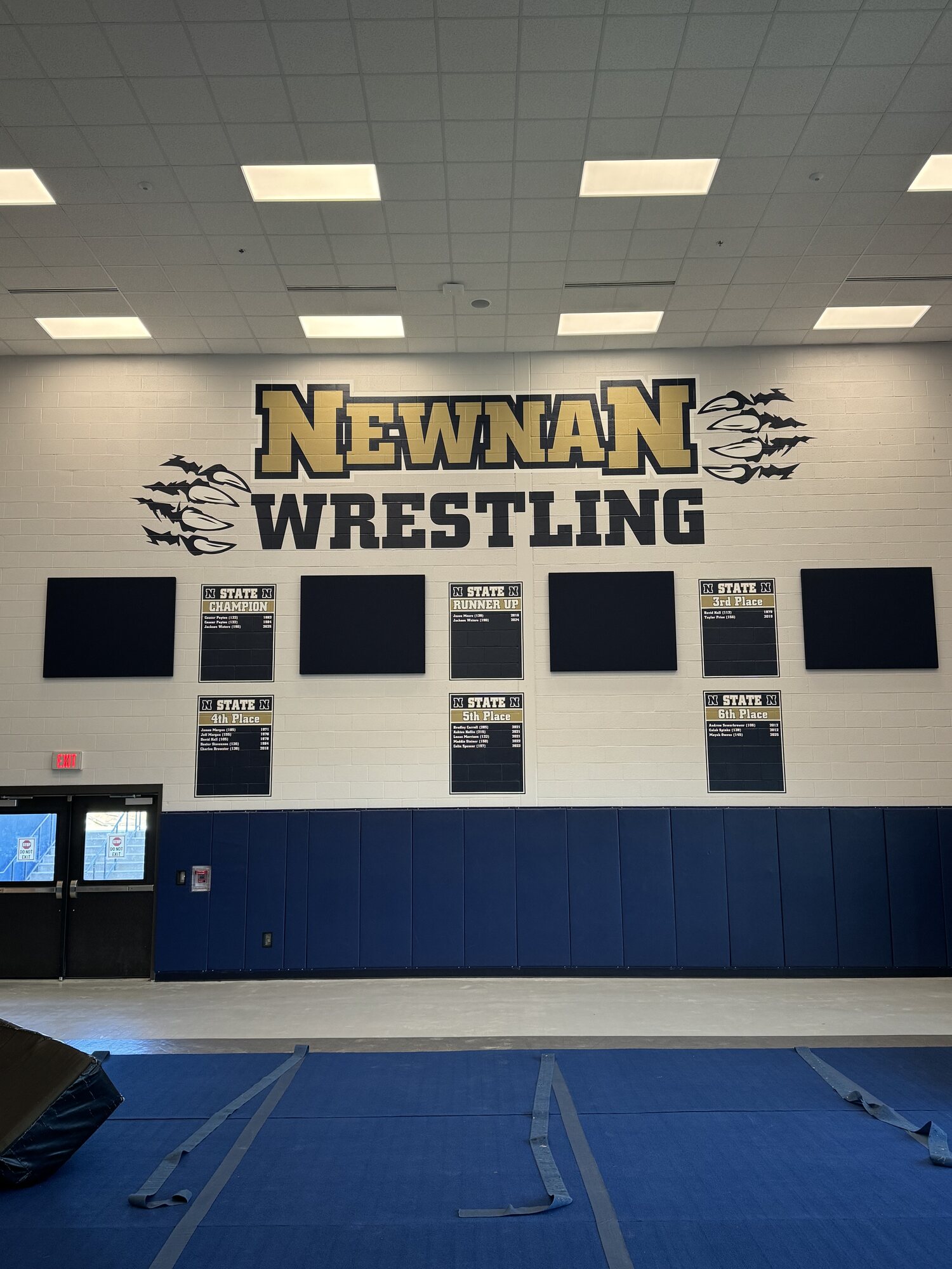 Newnan Wrestling wall graphics in gold and black with claw marks and state placement record boards on a gym wall